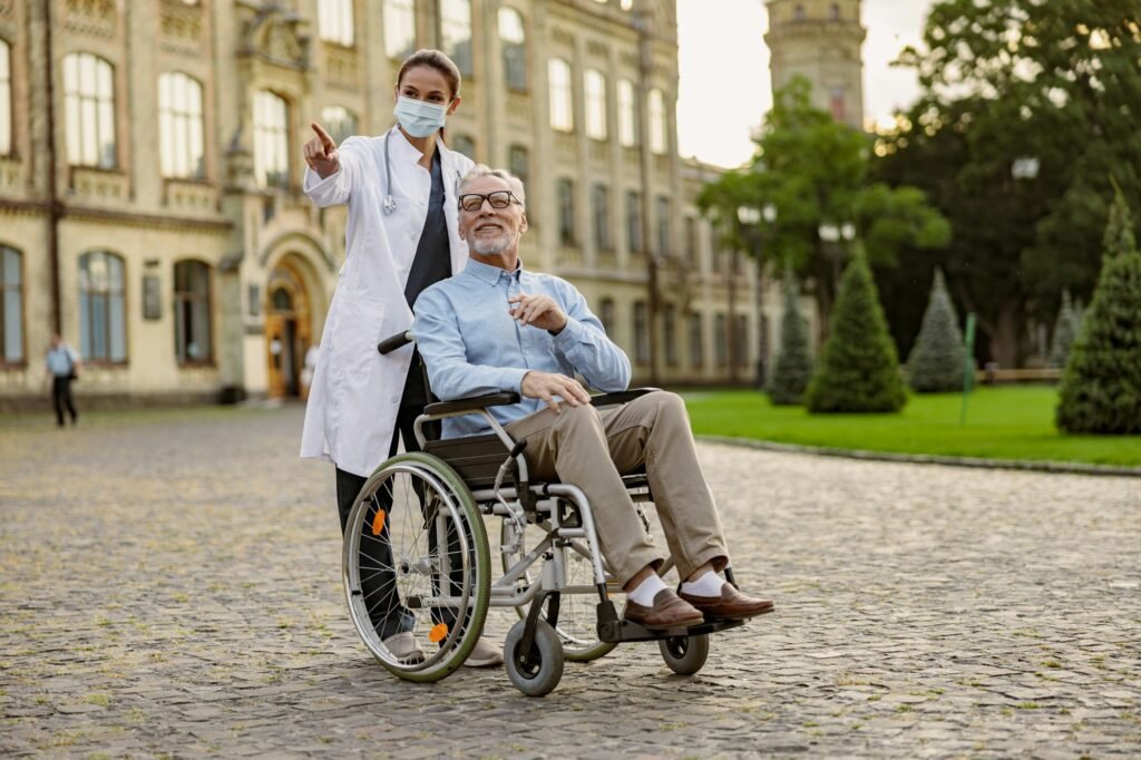 Full length shot of caring young nurse in protective mask taking care of senior man handicapped